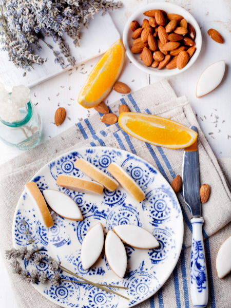 a beautiful round and white and blue painted plate with delicious leaf shaped cookies on it with a side of almonds and orange slices