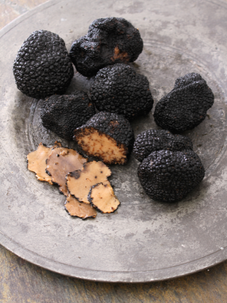 a metal round plate with black truffles on it one truffle is sliced exposing the inside